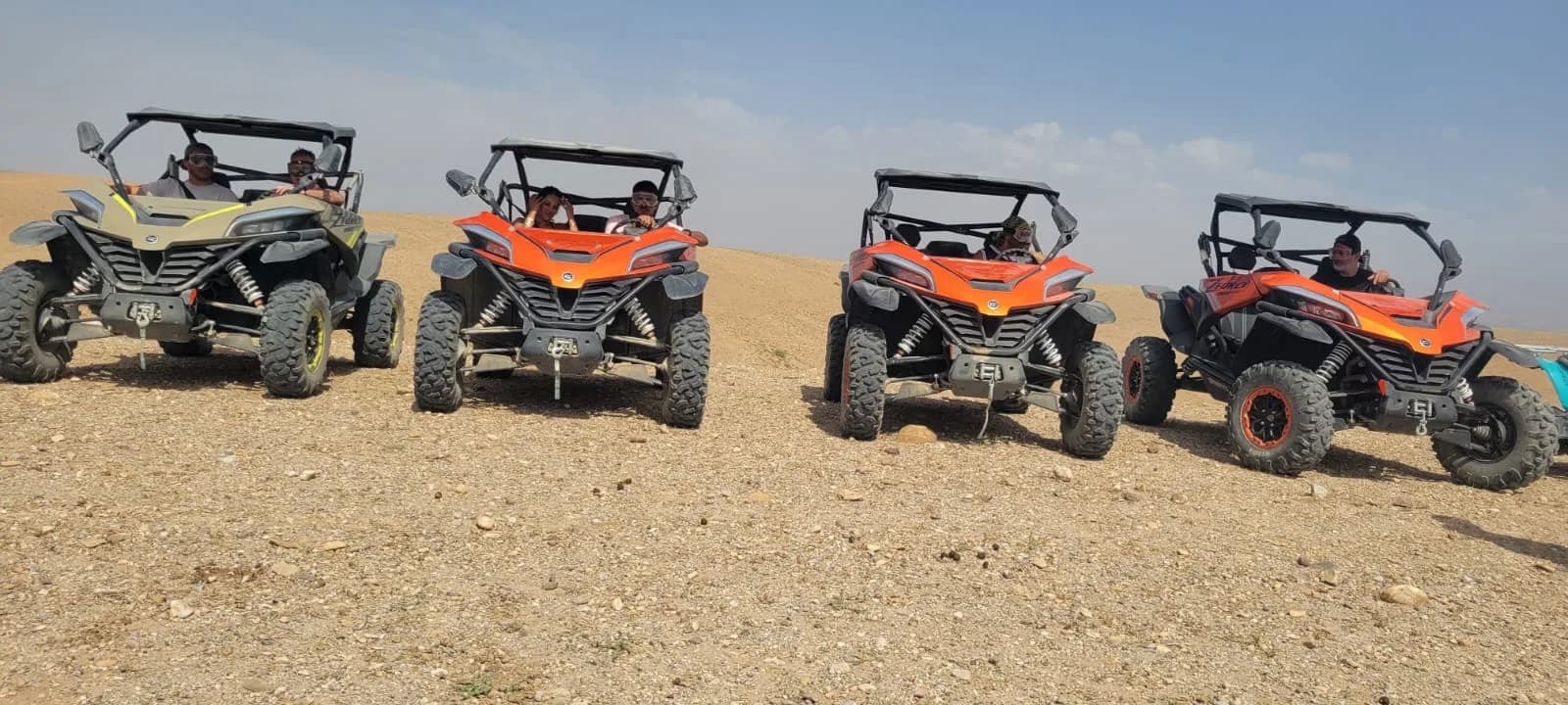 A line of off-road buggies with riders parked across the open Agafay Desert