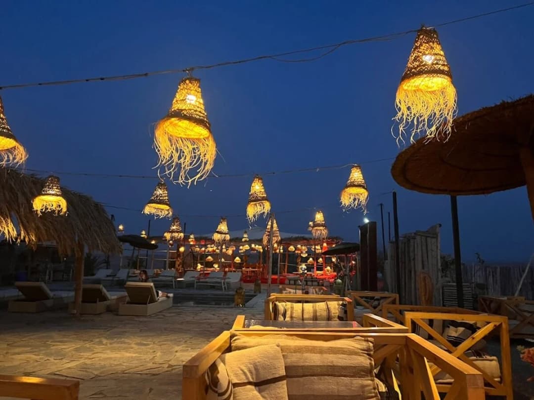 A desert dinner camp at dusk, lit by large woven lanterns hanging over the seating area