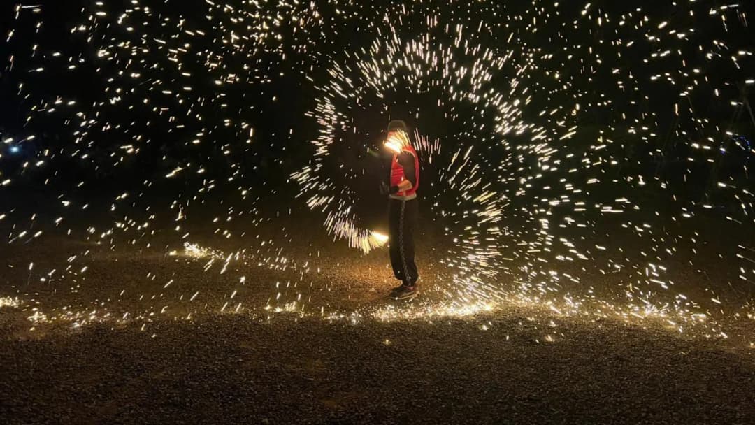 A performer spinning a shower of golden sparks in a circle on dark ground at night