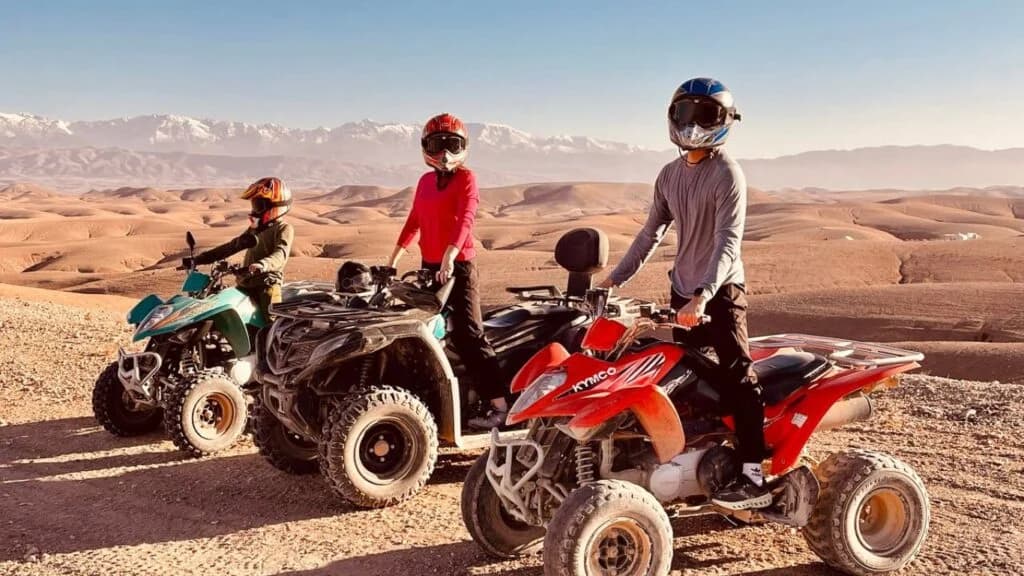 Guests in helmets with their quad bikes on a stony hill in the Agafay Desert, the Atlas Mountains behind