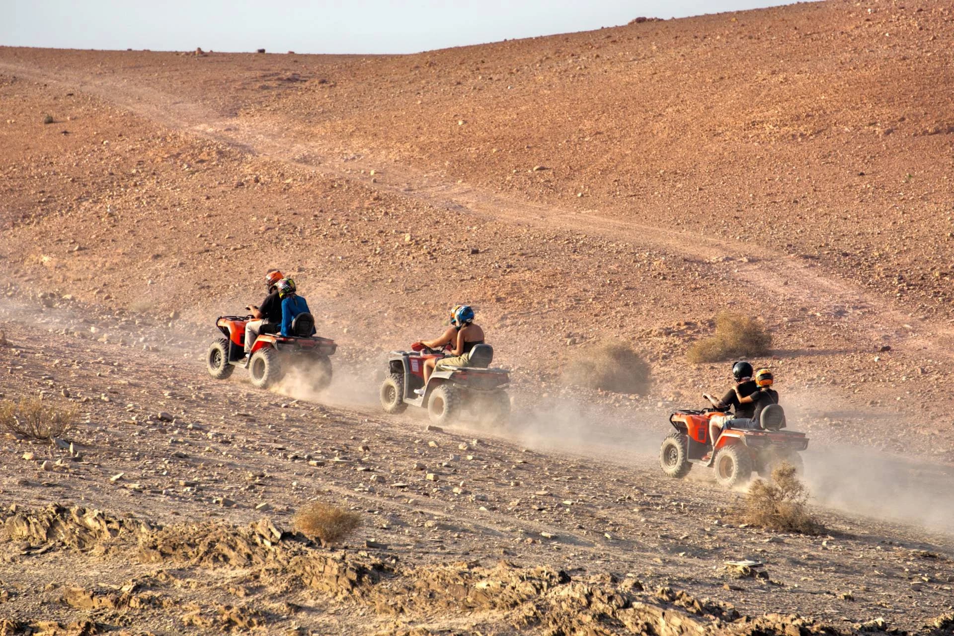 Trois quads soulèvent la poussière en montant une pente caillouteuse du désert d'Agafay