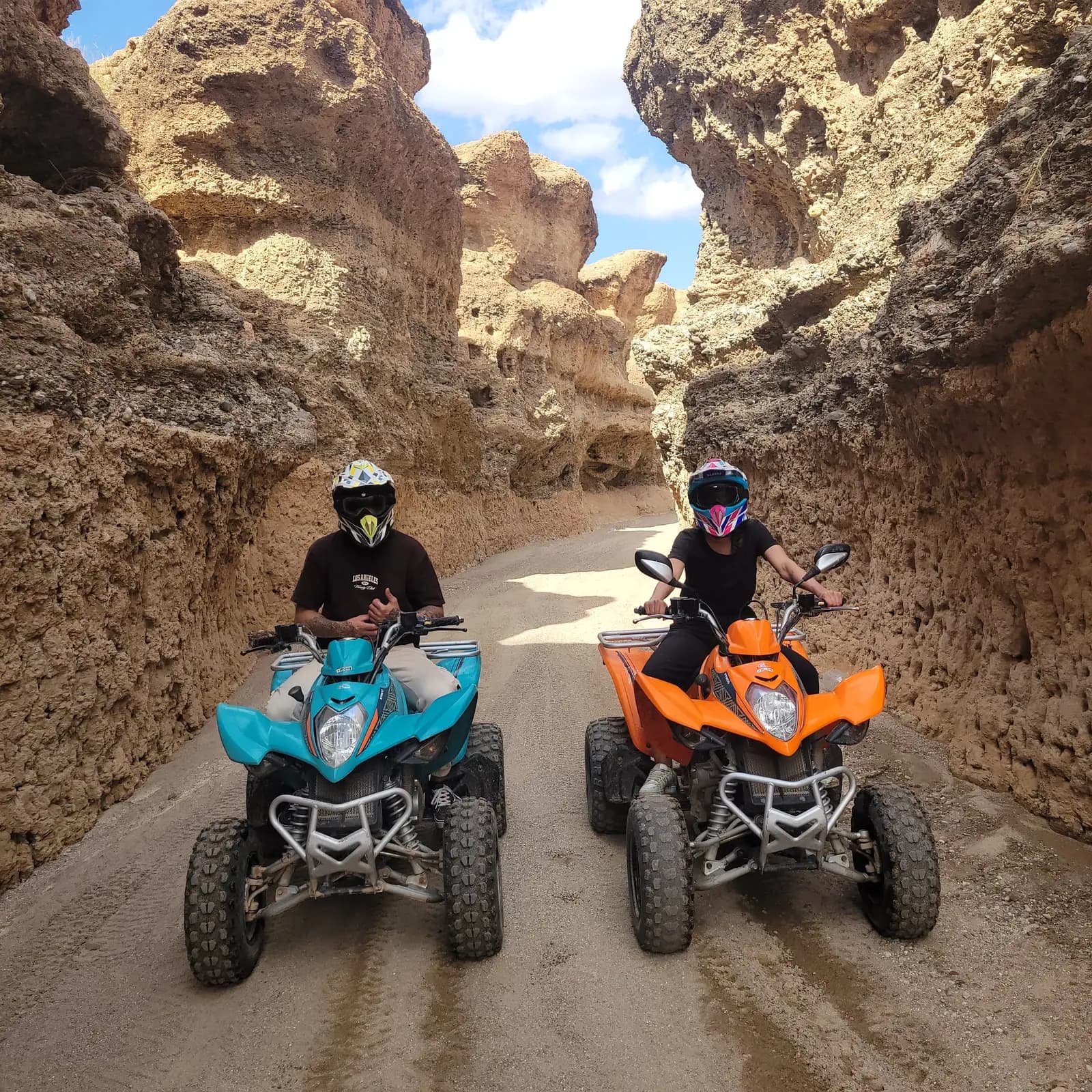 Two quad bike riders facing the camera side by side in a narrow Agafay Desert canyon