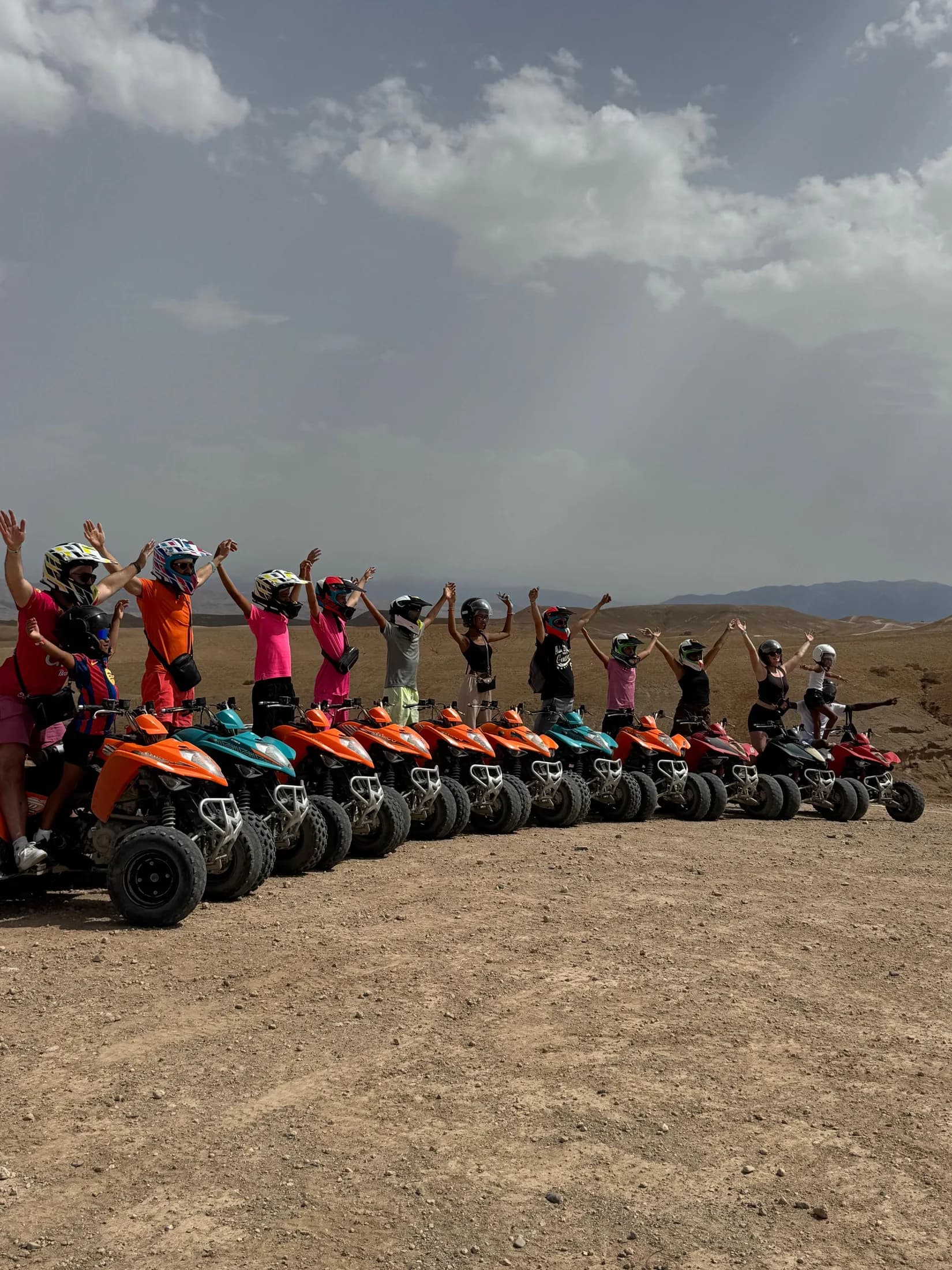 A group of guests with quad bikes raising their hands together in the Agafay Desert