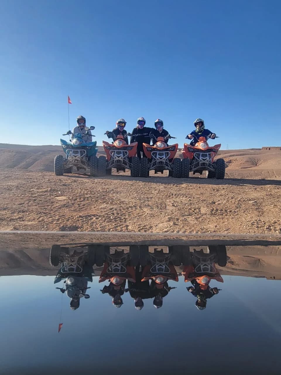 Quad bikes with riders lined up in the desert, reflected in a still pool of water