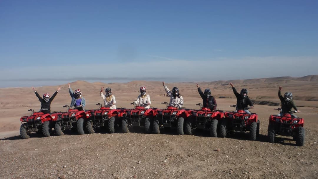 A row of riders in helmets with red quads, arms raised, on a stony plateau in the Agafay Desert