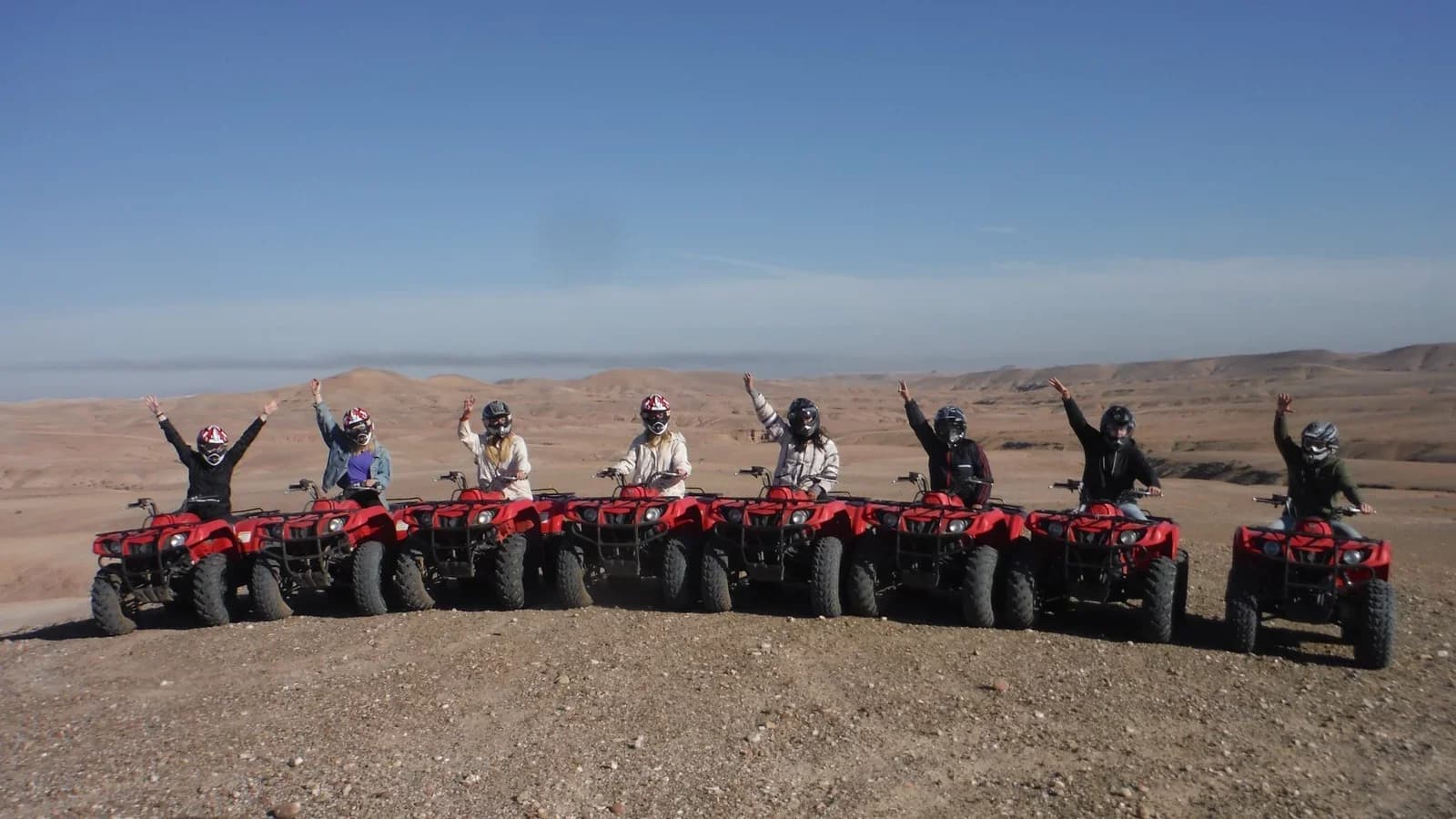 Une rangée de pilotes casqués avec des quads rouges sur un plateau caillouteux du désert d'Agafay